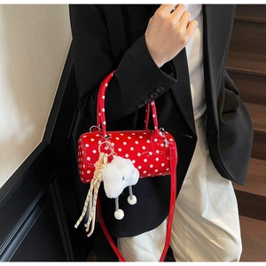 Close-up of a red polka dot barrel bag with a plush cloud charm and white strap