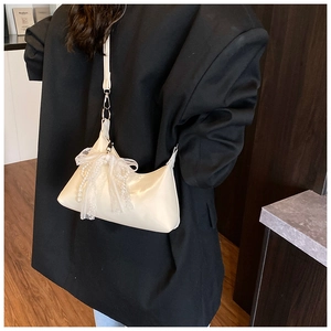 Détail du sac hobo blanc crème avec nœud en dentelle et breloque perle sur un blazer