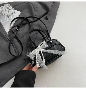 Detail view of a black lychee texture mini bag with white lace and pearl bow decoration
