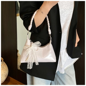 Détail du sac à main rose clair en cuir verni avec anse tressée et nœud en dentelle