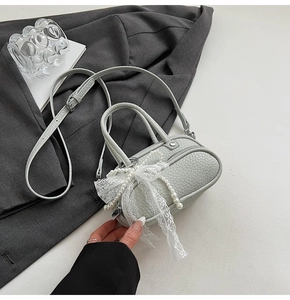 Detail of light green leather mini bag with lace bow and pearl chain on a grey blazer