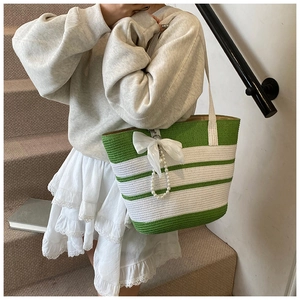 Detalle de bolso tejido a rayas verdes y blancas con lazo blanco y colgante de perlas