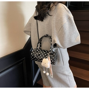 Close-up of a black polka dot cylindrical bag with a white plush cloud charm on a strap