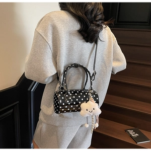 Close-up of a polka dot cylinder bag with a white plush cloud charm and hand strap