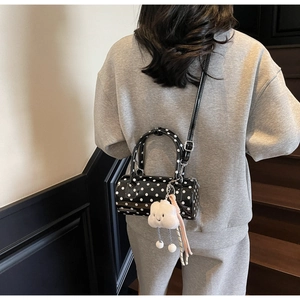 Close-up of a polka dot cylinder crossbody bag with a plush cloud charm on a model