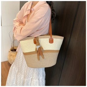 Close-up of woven straw tote bag with brown leather handles and cute bunny pendant