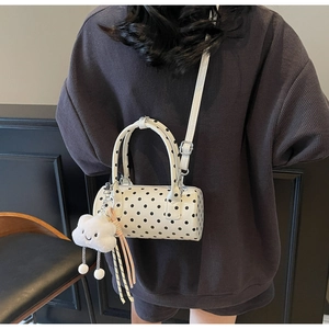 Polka dot cylinder bag with plush cloud charm shown on model in minimalist setting