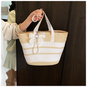 Detalle del bolso de paja a rayas con colgante de perlas y lazo para vacaciones de verano