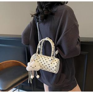 Detail of polka dot cylinder bag with a white plush cloud charm and slim strap
