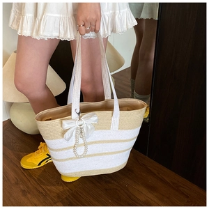 Detalle de un bolso de paja a rayas con lazo de gasa blanca y colgante de perlas elegante