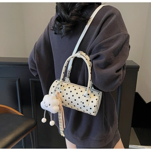 Close-up of a white polka dot cylinder bag with a cute cloud plush charm on strap