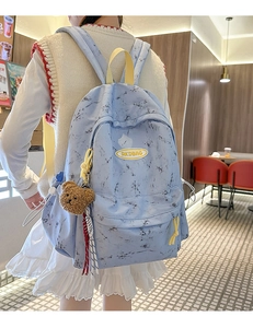 Detalle de mochila con estampado de mármol, asa amarilla y colgante de oso en modelo