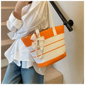Detalle del bolso de paja con rayas naranjas con lazo blanco y adorno de perlas