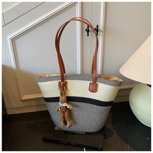 Detail of large woven beach tote with striped patterns and brown leather handles
