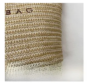 Detailed close-up of woven straw texture with embroidered BAG lettering on a beach tote bag