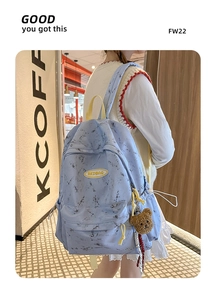 Detalle de mochila azul claro efecto mármol con logo y colgante de oso de peluche