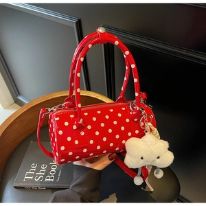 Close-up of a red polka dot barrel bag with a plush cloud charm on a black seat