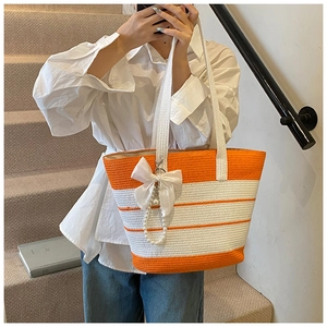 Dettaglio borsa tote in paglia a righe arancioni con fiocco bianco e pendente di perle