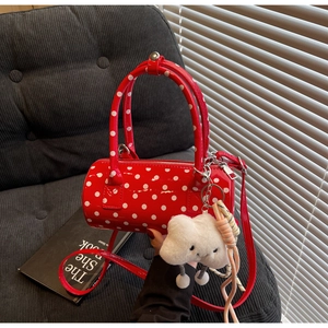 Close-up of red polka dot barrel bag with a plush cloud charm on a velvet sofa