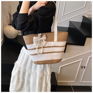 Detalle del bolso tote de paja a rayas con lazo blanco y elegante colgante de perlas