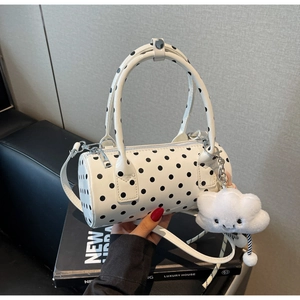Close-up of a white polka dot barrel bag with a plush cloud charm and top handles