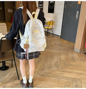 Detalle de mochila blanca con diseño de mármol, correas amarillas y colgante de oso