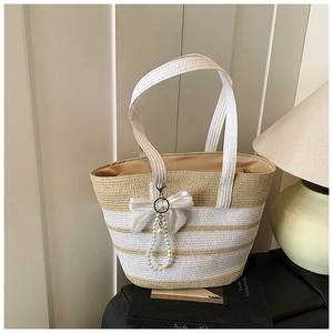 Detalle de bolsa de paja a rayas con lazo de satén blanco y elegante colgante de perlas