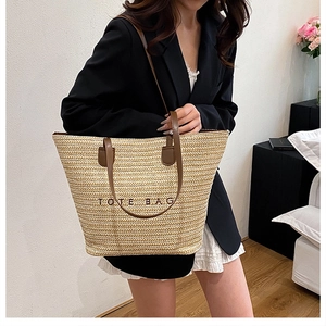 Detail of the woven tote bag showing beige straw texture and brown leather handle