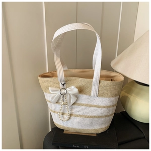 Dettaglio borsa di paglia a righe con fiocco di seta bianca e catena di perle elegante