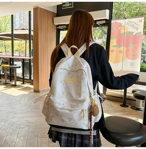 Detalle de la mochila blanca con efecto mármol, asa amarilla y colgante de felpa al costado