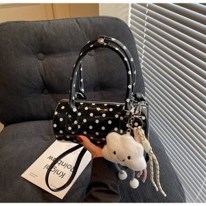 Close-up of glossy black polka dot cylinder bag with plush cloud charm and strap