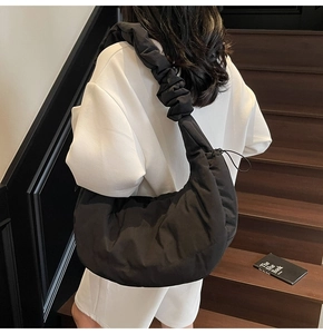 Detail view of a black quilted cloud dumpling bag worn by a model on wooden stairs