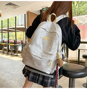 Detalle de mochila con patrón de mármol blanco, correas amarillas y colgante de peluche