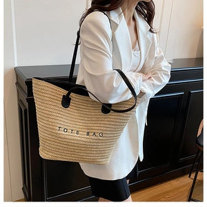 Fashion straw tote bag with black leather handles shown as a crossbody on a model
