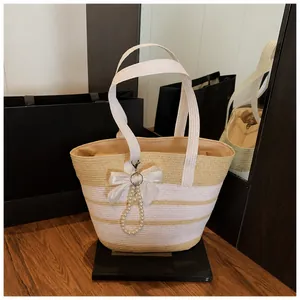 Detalle de bolso de paja a rayas con lazo de encaje blanco y colgante de perlas