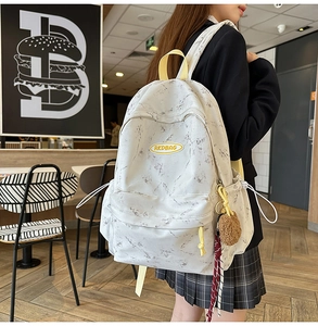 Detalle de la mochila con estampado de mármol, parche amarillo y colgante de peluche