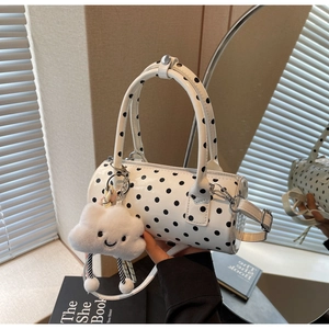 Detailed view of white polka dot cylinder bag with cute cloud charm and silver hardware