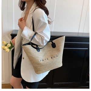 Detailed view of beige woven tote bag with black leather handles and printed text logo