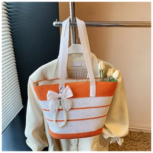 Detalle del bolso de paja a rayas con lazo de malla blanca y colgantes de perlas para playa