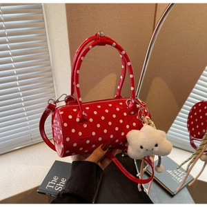 Close-up of red polka dot cylinder bag featuring a white plush cloud charm and strap