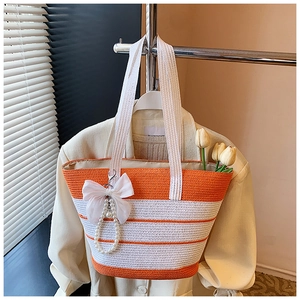 Detalle del bolso de paja a rayas naranjas con lazo blanco y colgante de perlas