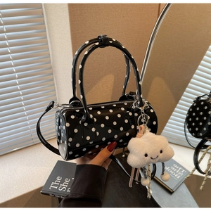 Close-up of black and white polka dot cylindrical bag with plush cloud charm and strap