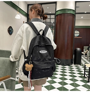 Detalle de mochila negra con estampado de mármol, correas ajustables y colgante de oso