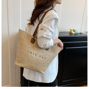 Close-up of woven straw tote bag featuring brown TOTE BAG embroidery and leather handles