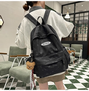 Detalle de mochila negra de nailon con patrón de salpicaduras blancas y llavero de oso