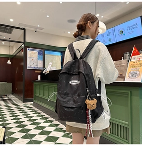Detalle de mochila informal con estampado de mármol y colgante de oso de peluche en café