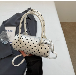 Detailed close-up of a white cylindrical handbag with black polka dots and shiny finish
