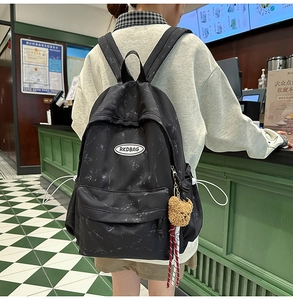 Detalle de mochila negra con estampado de mármol y un bonito colgante de osito