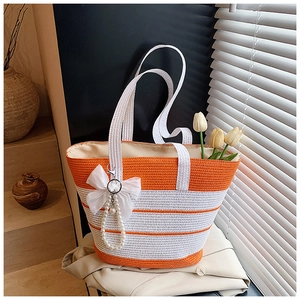 Detalle del bolso tote de paja a rayas naranjas y blancas con colgante de lazo y perlas