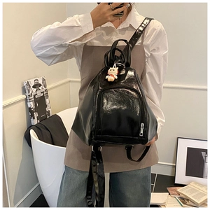 Detailed view of black glossy patent leather backpack with front zipper and top handle